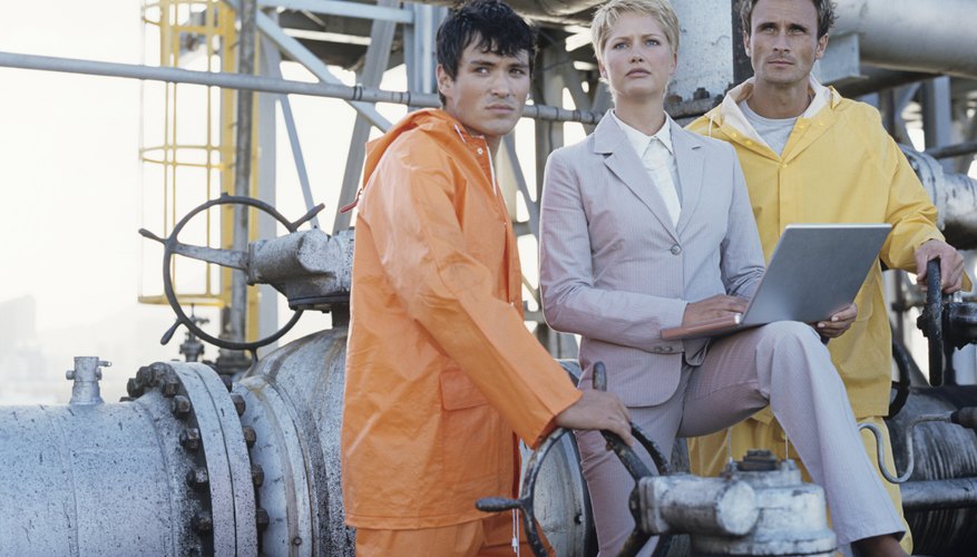 Business woman and two oil refinery workers,woman holding laptop