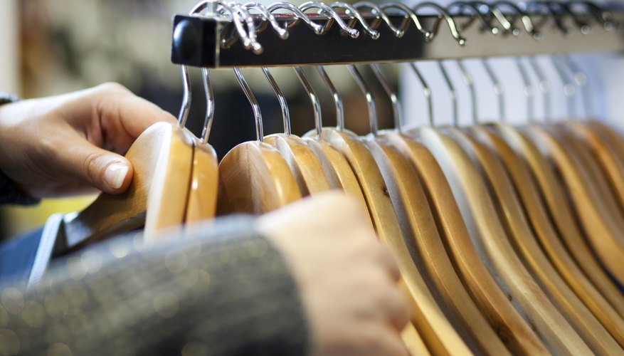 A woman's hands sorting through clothes hanging on a rack.