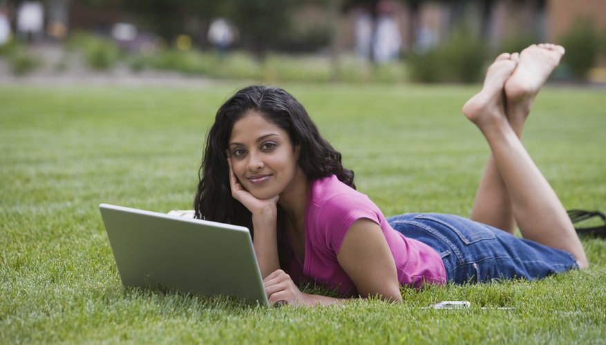 Young student working on laptop while laying on campus lawn.