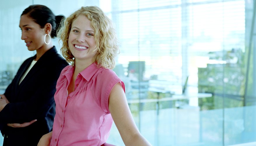 Woman standing with female colleague in office, smiling, portrait