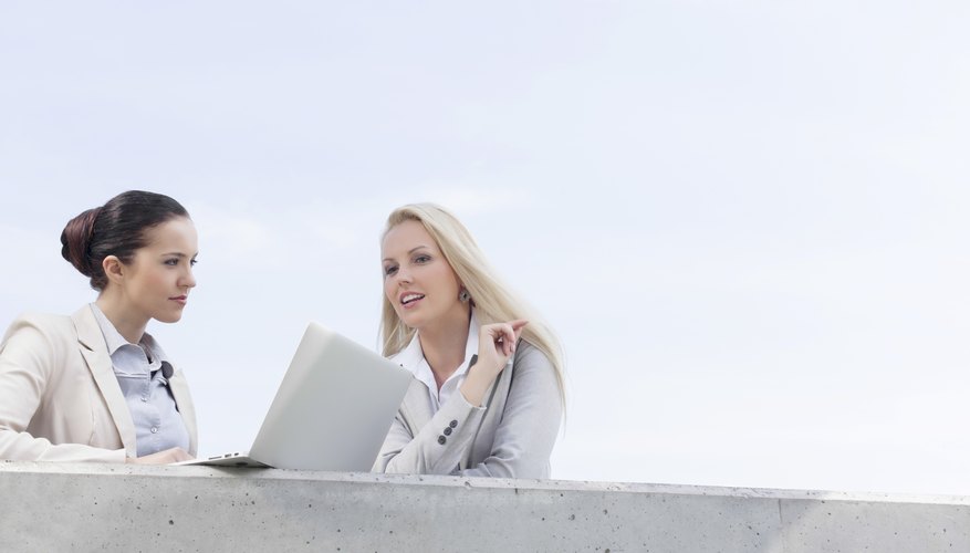Low angle view of young businesswomen with laptop discussing while standing on terrace against sky