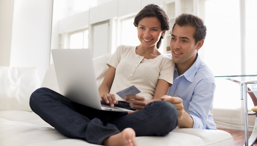 A pair of newlyweds on the couch with a laptop computer and a credit card.