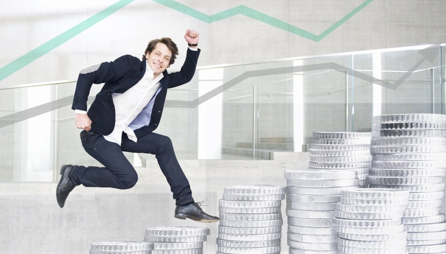 Young businessman jumping on front of stacks of silver coins and graph