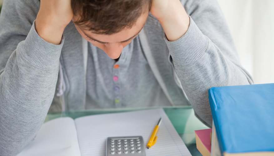 A student looks down at an empty notebook and a calculator on his desk. A student looks down at an empty notebook and a calculator on his desk.