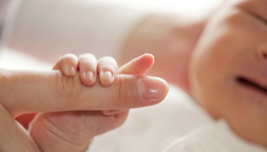 A close-up of a newborn holding a woman's finger. A close-up of a newborn holding a woman's finger.