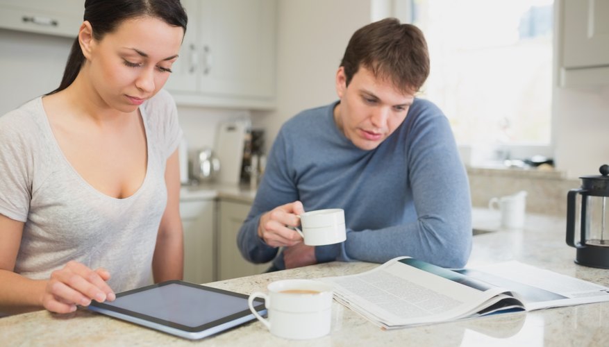 Two people reading from tablet pc and newspaper