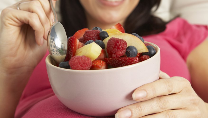 A pregnant woman reclines while eating a bowl of fruit. A pregnant woman reclines while eating a bowl of fruit.