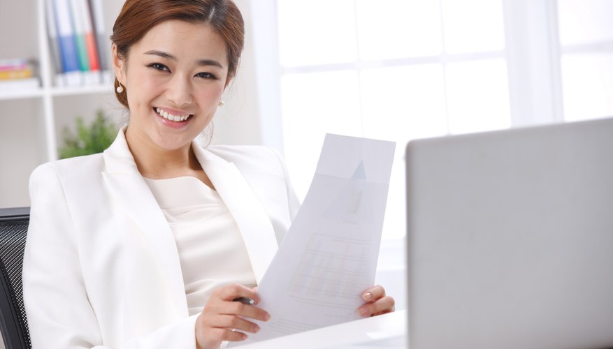 Young business lady holding paper in front of laptop