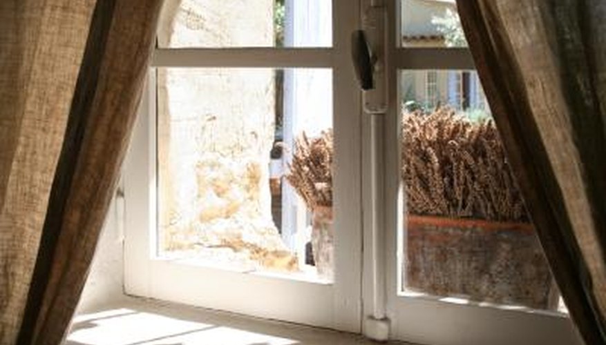 Unbleached muslin curtains inside a cottage window with lavender on the sill. Unbleached muslin curtains inside a cottage window with lavender on the sill.