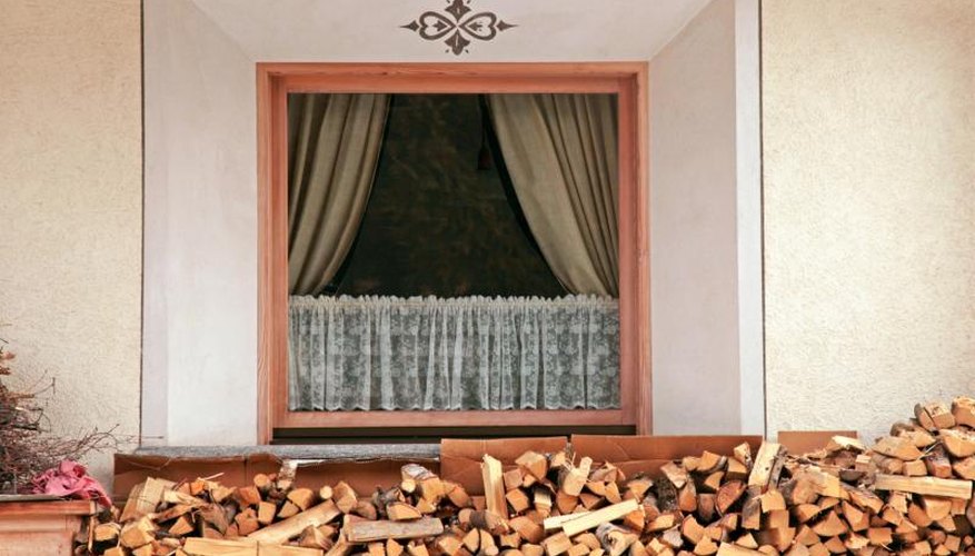 Cafe curtains inside the window above a wood pile. Cafe curtains inside the window above a wood pile.