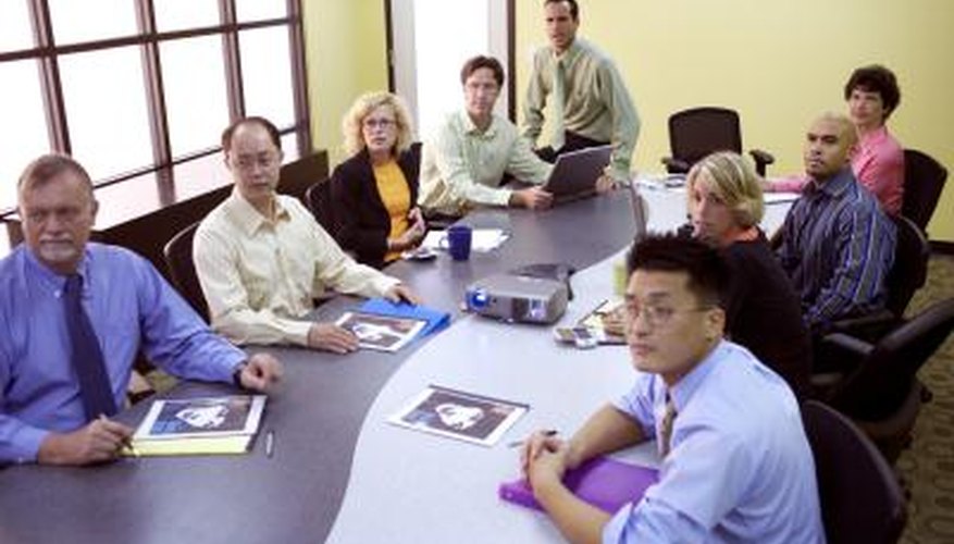Employees sit at a curved table that divides into two in a conference room. Employees sit at a curved table that divides into two in a conference room.